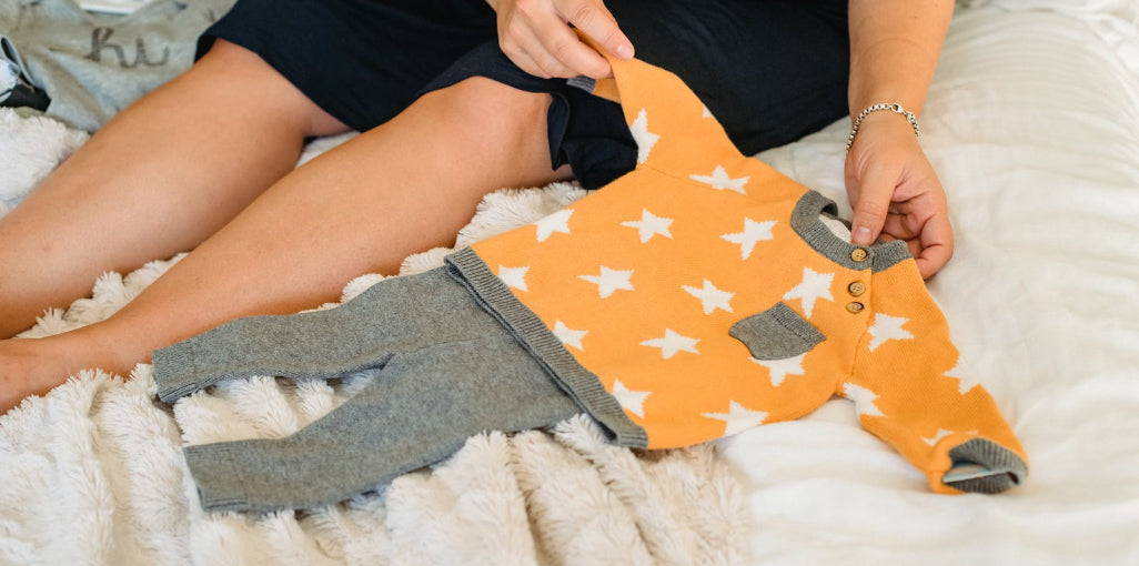 A person holding a cute, star - patterned baby outfit, representing thoughtful gifts for new moms to celebrate motherhood.
