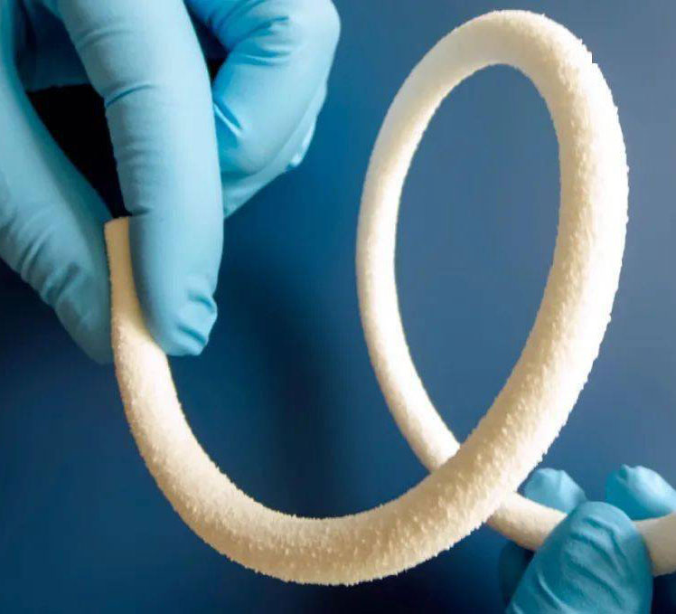 Hands in blue lab gloves holding a flexible, white artificial blood vessel made from silk