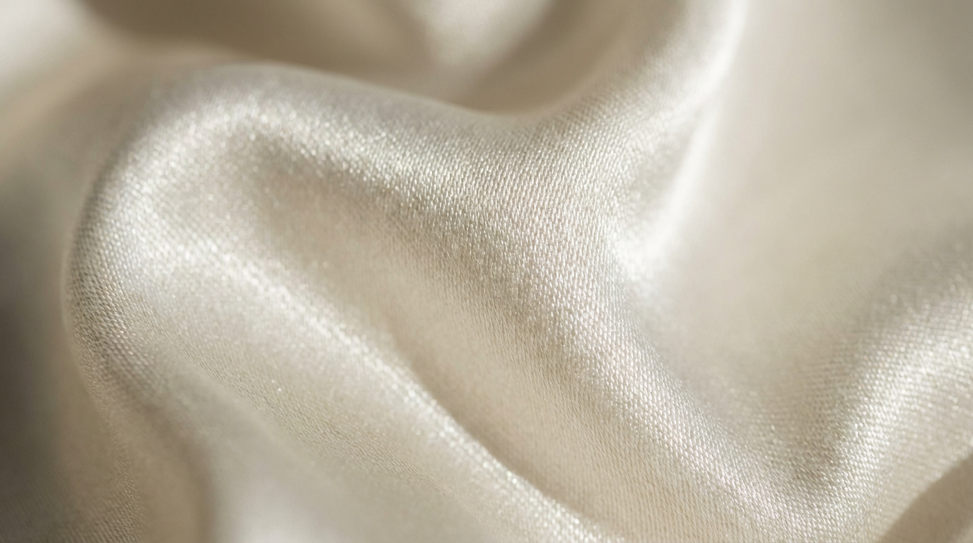 Close up of draped ivory silk fabric showing elegant folds and a shimmering smooth texture.