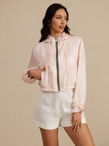 Woman wearing a cropped silk hooded jacket with zipper, pockets and ruffled cuffs