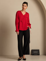 White silk V-neck blouse with long sleeves, pleated front, buttoned cuffs, and 3D rose detail